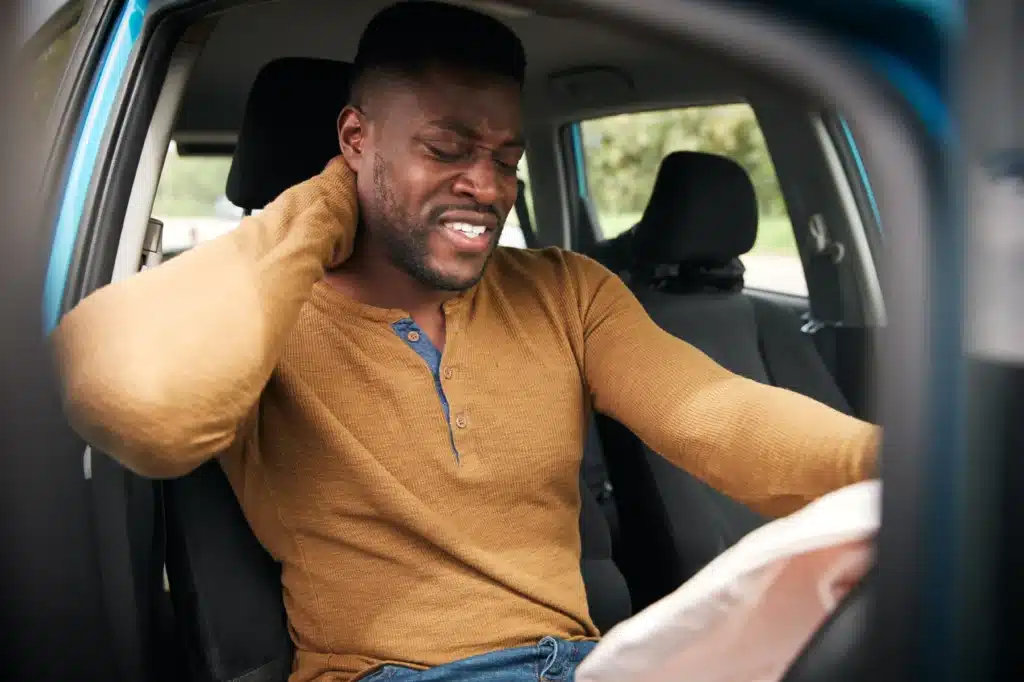 Driver in visible discomfort holding his neck after experiencing a car crash-related whiplash injury.