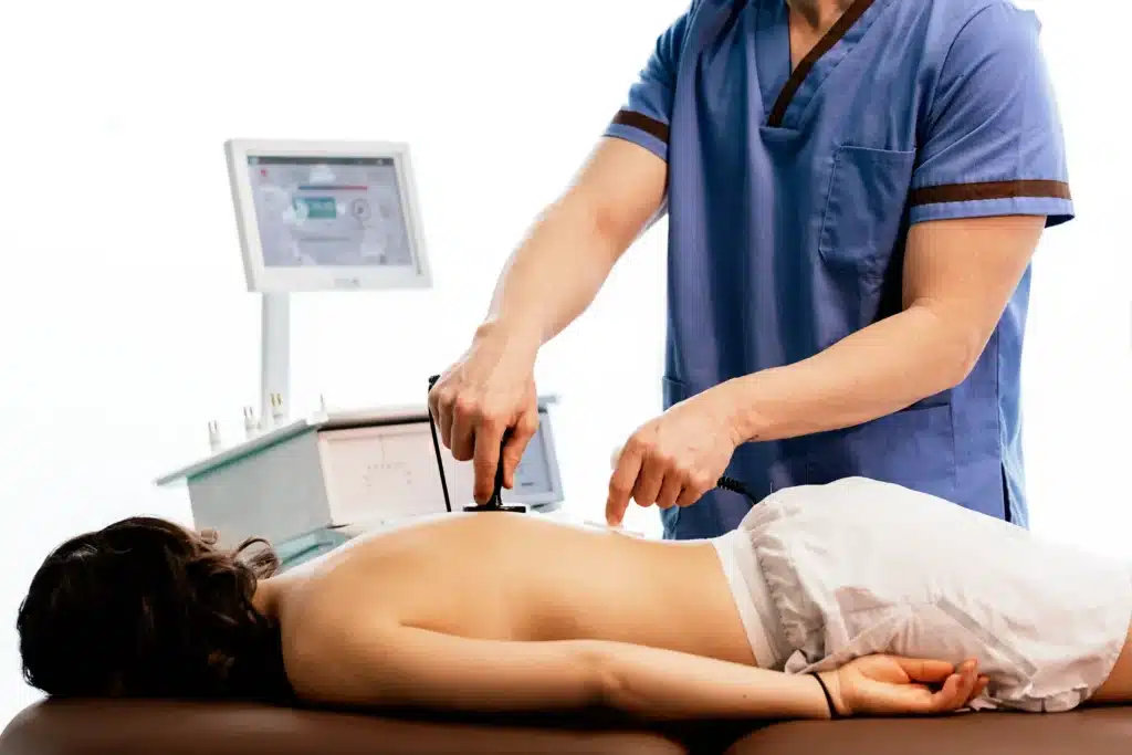 Physiotherapist using advanced equipment for back pain laser treatment on a female patient.