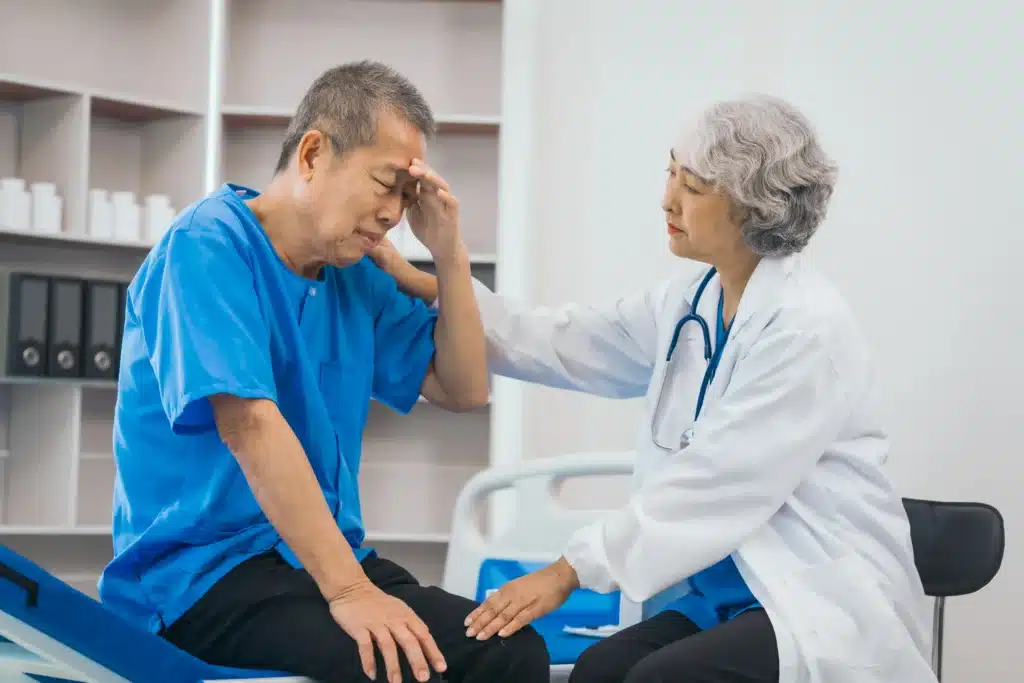 Asian female doctor comforting a senior male patient who appears to be in distress during a medical consultation.