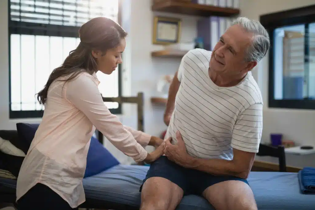 Senior male patient experiencing lower back pain while being examined by a female healthcare professional.