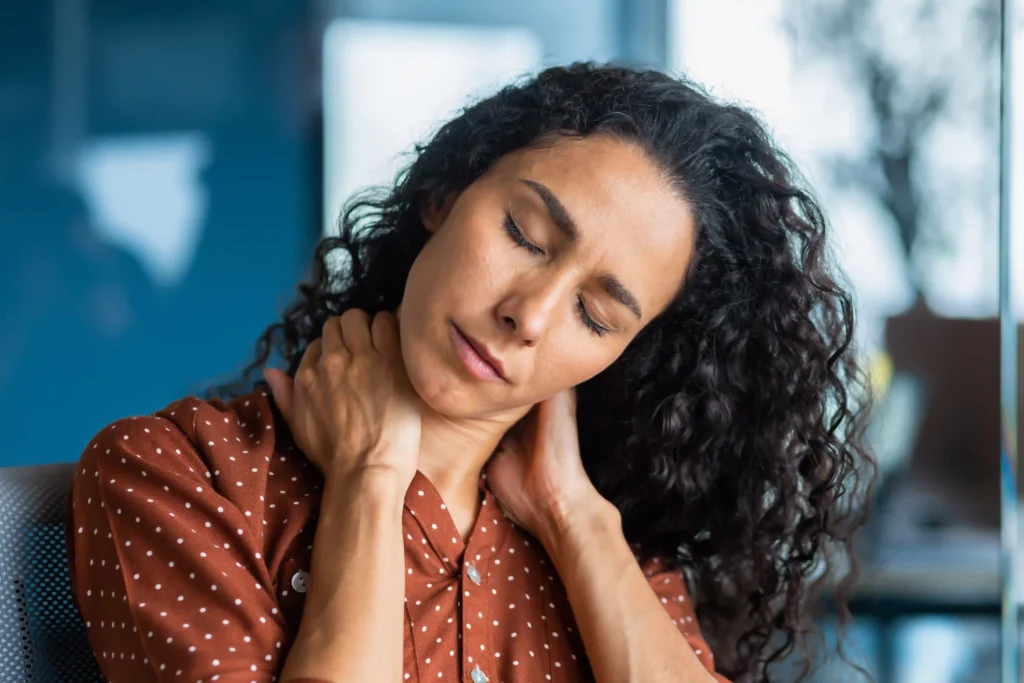 Woman massaging her neck at the office, highlighting discomfort that can be eased with neck pain laser treatment.