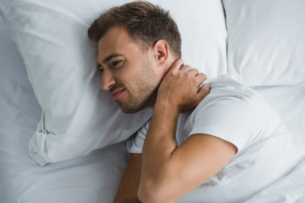 Top view of a young man lying in bed, suffering from neck pain.