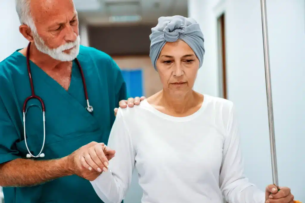 Elderly male doctor supporting a woman undergoing cancer treatment as she walks through a hospital hallway