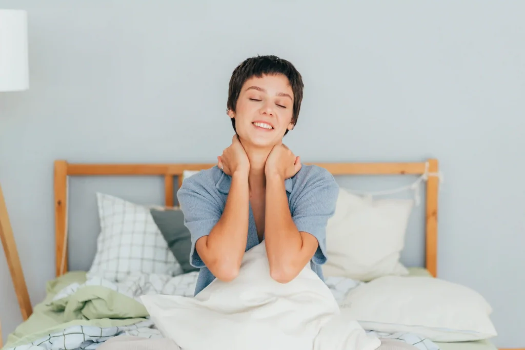 Brunette woman sitting in bed, massaging her neck to ease pain.