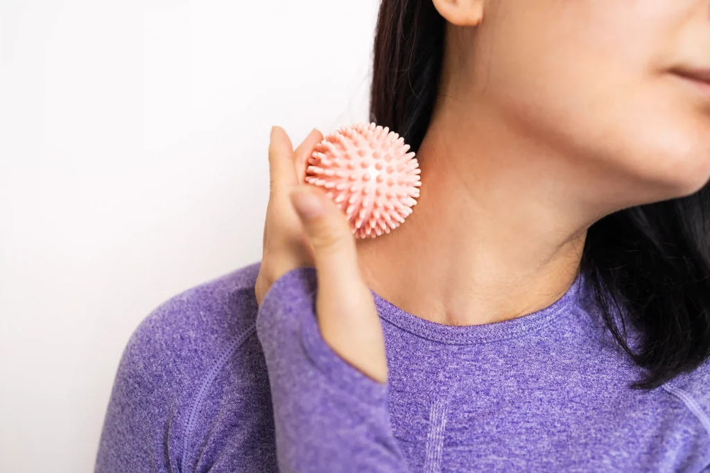 Woman in sportswear applying a massage ball on her neck for pain relief pressure points.