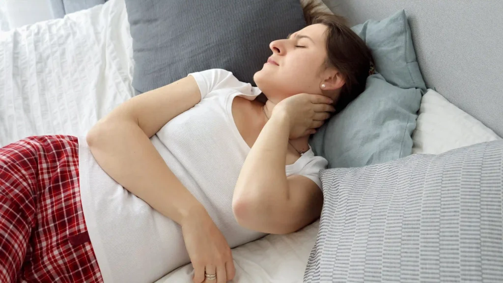 Young woman in pajamas holding her neck after waking up with stiffness.